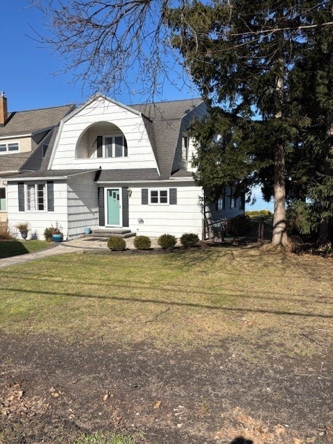 colonial inspired home featuring a front lawn, a gambrel roof, and a shingled roof