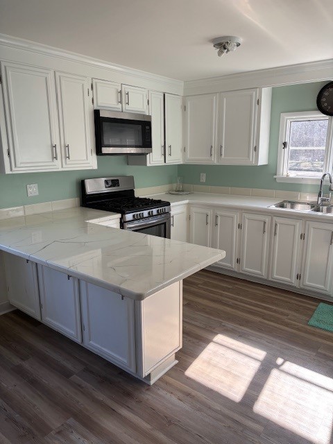 kitchen with a sink, stainless steel appliances, a peninsula, and white cabinets