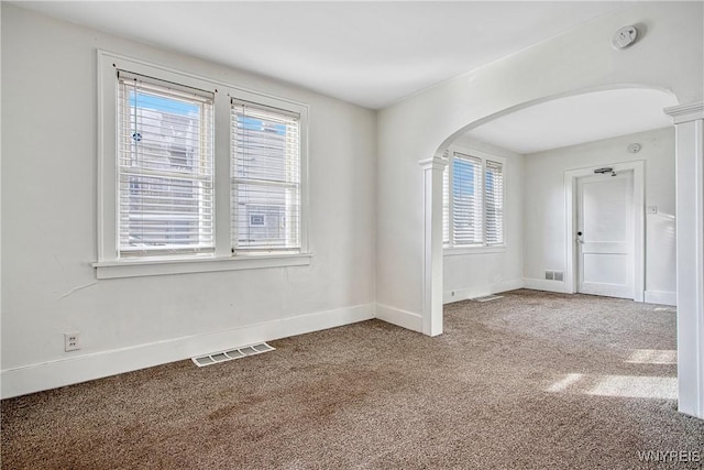 unfurnished room featuring arched walkways, visible vents, baseboards, and carpet floors