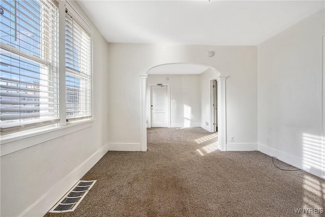 carpeted empty room with arched walkways, visible vents, baseboards, and decorative columns