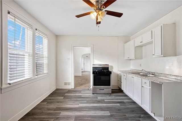 kitchen with a sink, baseboards, gas range, arched walkways, and dark wood-style flooring