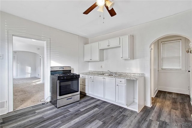 kitchen with dark wood finished floors, stainless steel gas range, arched walkways, white cabinetry, and a sink