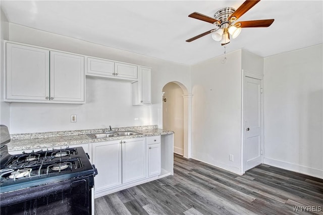 kitchen featuring arched walkways, gas stove, white cabinetry, and a sink