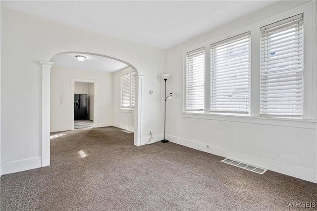 spare room with visible vents, ornate columns, carpet floors, baseboards, and arched walkways