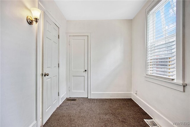 unfurnished room featuring visible vents, dark carpet, baseboards, and a healthy amount of sunlight