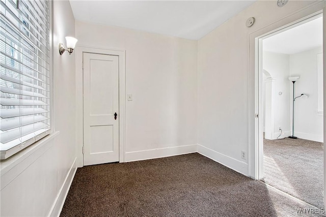 spare room featuring baseboards and dark carpet