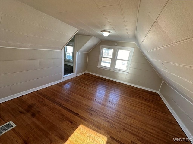 bonus room featuring visible vents, a textured ceiling, wood finished floors, baseboards, and vaulted ceiling