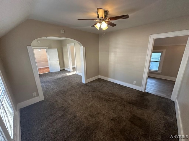 unfurnished room with arched walkways, baseboards, and dark colored carpet