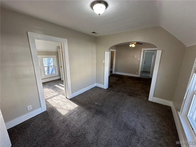unfurnished bedroom featuring arched walkways, visible vents, baseboards, and dark colored carpet