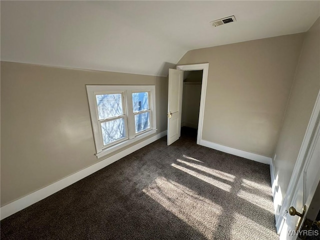 unfurnished bedroom with dark colored carpet, visible vents, lofted ceiling, and baseboards