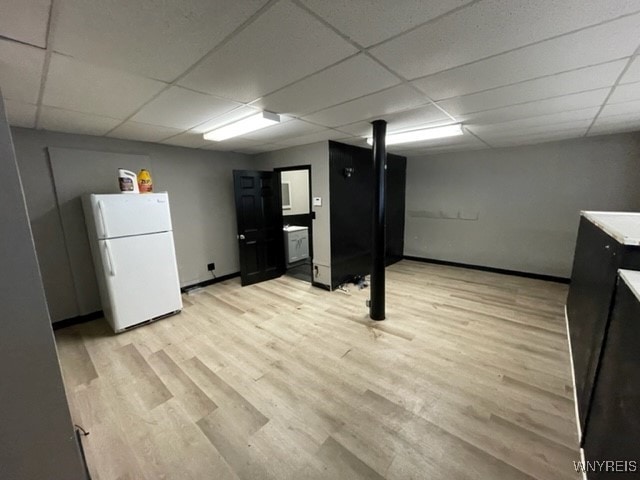 finished below grade area with a drop ceiling, baseboards, light wood-style floors, and freestanding refrigerator