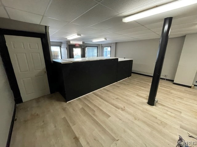 below grade area with a drop ceiling, light wood-style flooring, and a healthy amount of sunlight