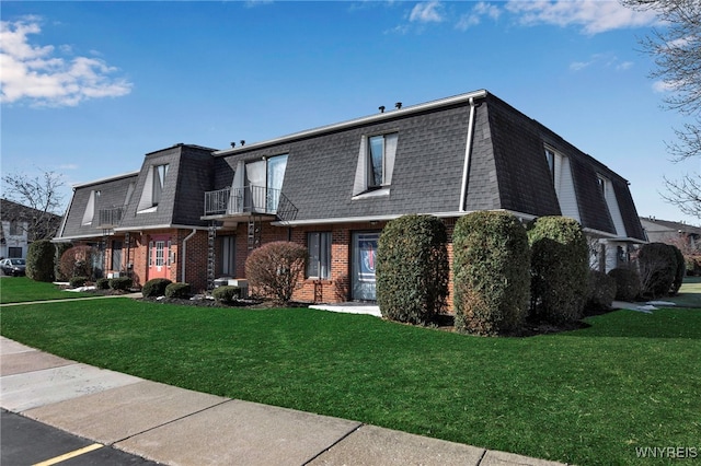 view of front of house featuring a front lawn, mansard roof, brick siding, and roof with shingles