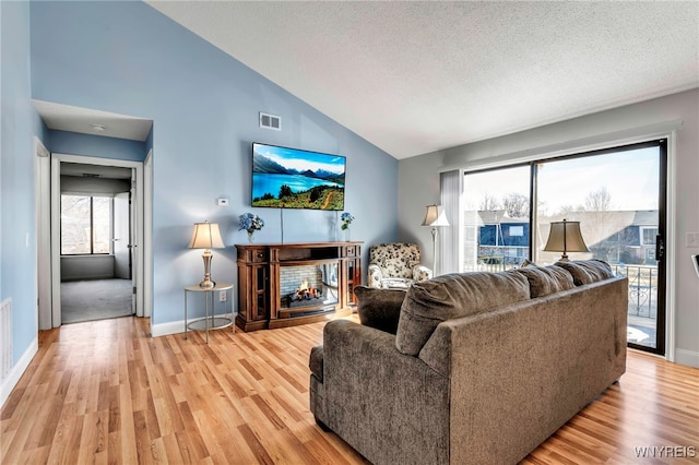 living area featuring visible vents, baseboards, a multi sided fireplace, light wood-style floors, and a textured ceiling