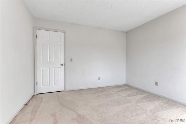 empty room with a textured ceiling, baseboards, and light carpet