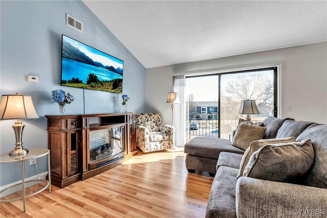 living room with visible vents, a textured ceiling, wood finished floors, a fireplace, and vaulted ceiling