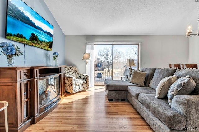 living area featuring a chandelier, a glass covered fireplace, a textured ceiling, and wood finished floors