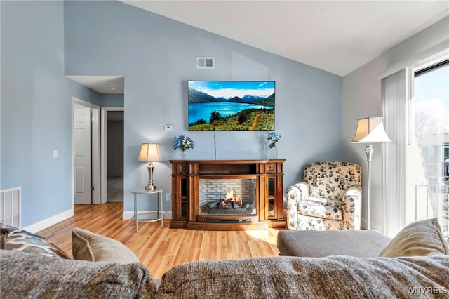 living area with visible vents, lofted ceiling, a lit fireplace, and wood finished floors