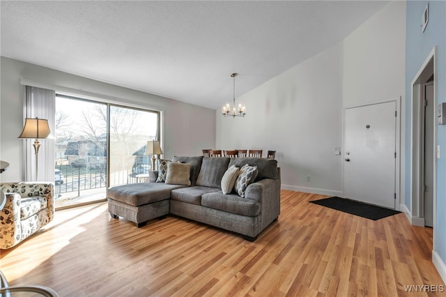 living area featuring visible vents, a textured ceiling, light wood-style floors, baseboards, and a chandelier