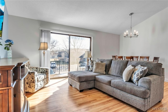 living area featuring a chandelier, light wood finished floors, a textured ceiling, and lofted ceiling