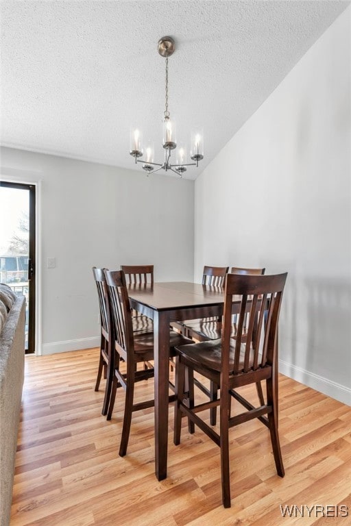 dining area featuring baseboards, light wood-style flooring, a textured ceiling, and an inviting chandelier