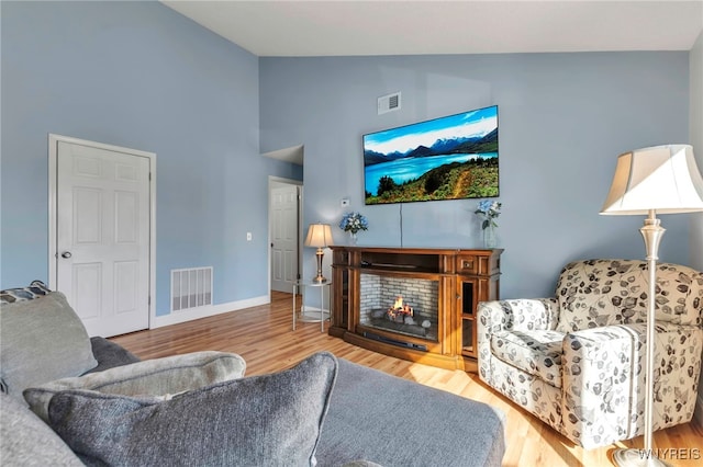 living area featuring visible vents, baseboards, a warm lit fireplace, and wood finished floors