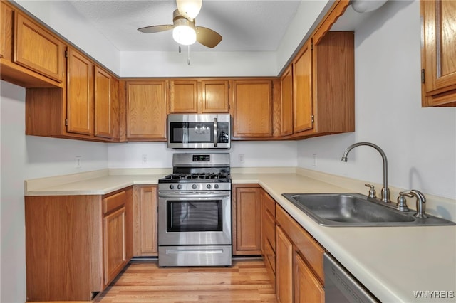 kitchen featuring light wood finished floors, brown cabinets, appliances with stainless steel finishes, and a sink