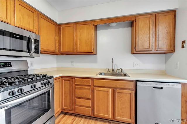 kitchen with brown cabinetry, a sink, stainless steel appliances, light countertops, and light wood-style floors