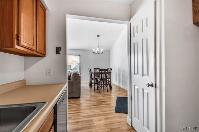 kitchen featuring brown cabinetry, a sink, dishwasher, a notable chandelier, and light wood-type flooring