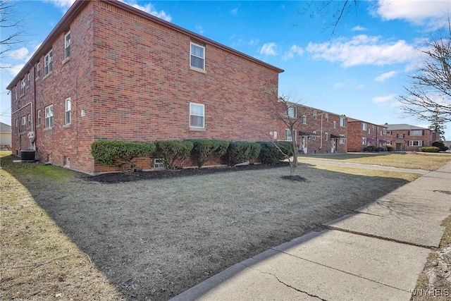 view of side of property featuring brick siding, central air condition unit, and a yard