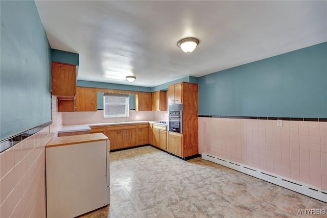 kitchen with light countertops, stainless steel oven, baseboard heating, wainscoting, and tile walls