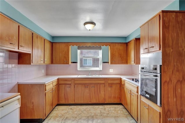 kitchen with a sink, light countertops, dishwasher, stainless steel oven, and backsplash