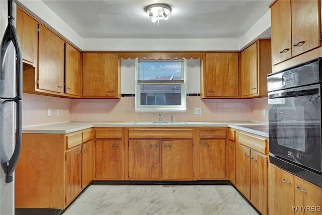 kitchen with freestanding refrigerator, a sink, light countertops, black oven, and marble finish floor