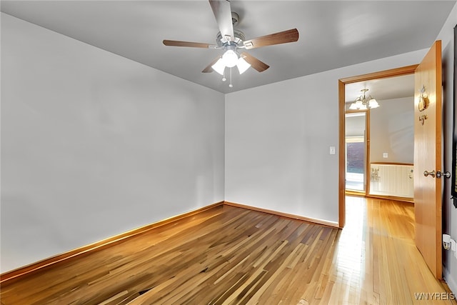 empty room with light wood-style flooring, ceiling fan with notable chandelier, and baseboards