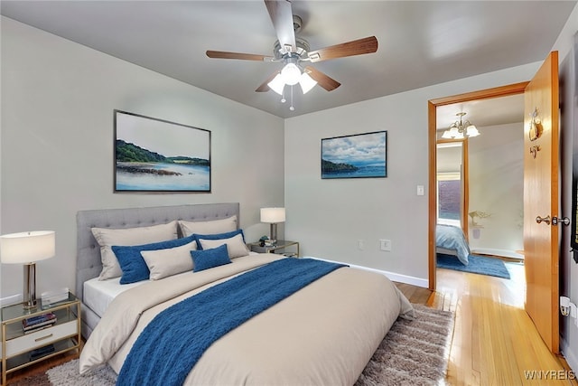 bedroom with hardwood / wood-style flooring, ceiling fan with notable chandelier, and baseboards