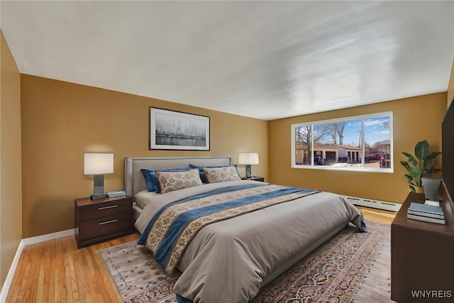 bedroom with a baseboard heating unit, baseboards, and light wood finished floors