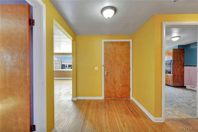 hallway featuring a baseboard heating unit, baseboards, and wood finished floors