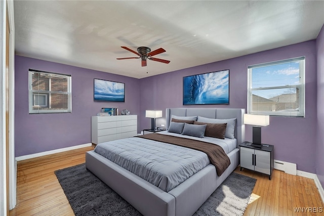 bedroom featuring baseboard heating, ceiling fan, light wood-type flooring, and baseboards