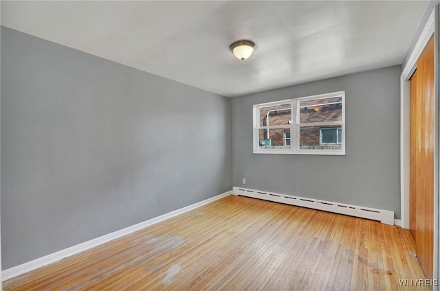 spare room featuring a baseboard heating unit, baseboards, and hardwood / wood-style floors