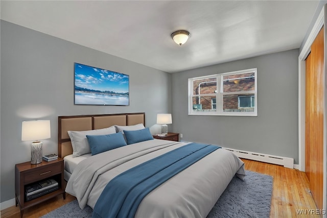 bedroom featuring a baseboard heating unit, baseboards, and light wood-type flooring