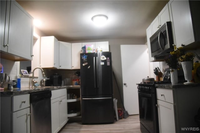 kitchen featuring backsplash, black appliances, light wood-type flooring, and dark stone counters