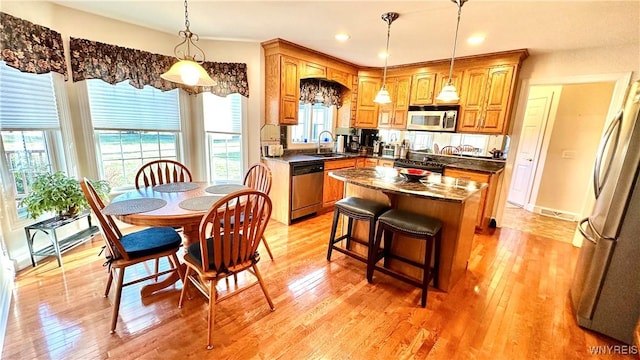 kitchen with dark countertops, a kitchen island, light wood-style flooring, stainless steel appliances, and a sink