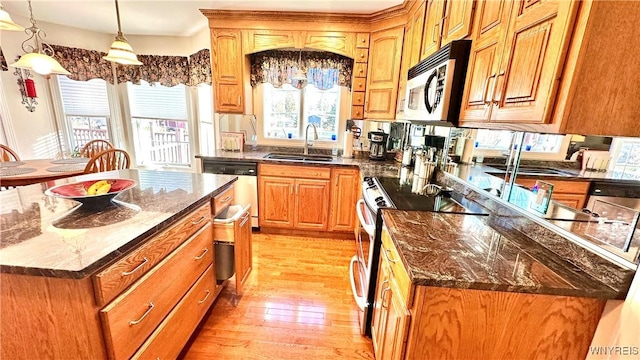 kitchen featuring a kitchen island, dark stone counters, light wood-type flooring, appliances with stainless steel finishes, and a sink