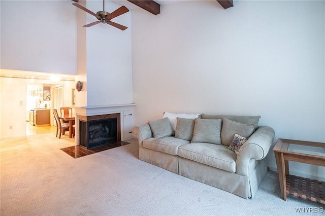 living area featuring beam ceiling, high vaulted ceiling, a fireplace with flush hearth, a ceiling fan, and carpet