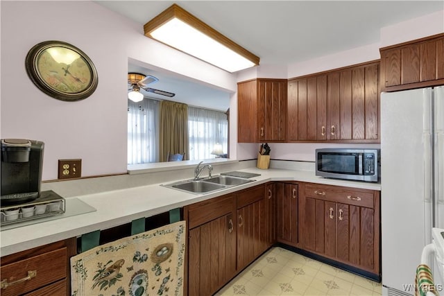 kitchen with stainless steel microwave, light floors, light countertops, freestanding refrigerator, and a sink