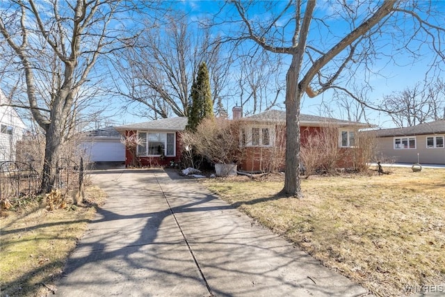 single story home with an outdoor structure, concrete driveway, brick siding, and a chimney