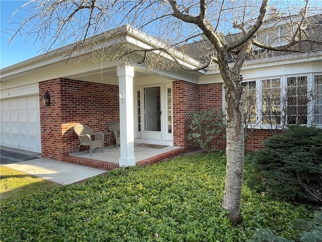 property entrance with brick siding, covered porch, and an attached garage