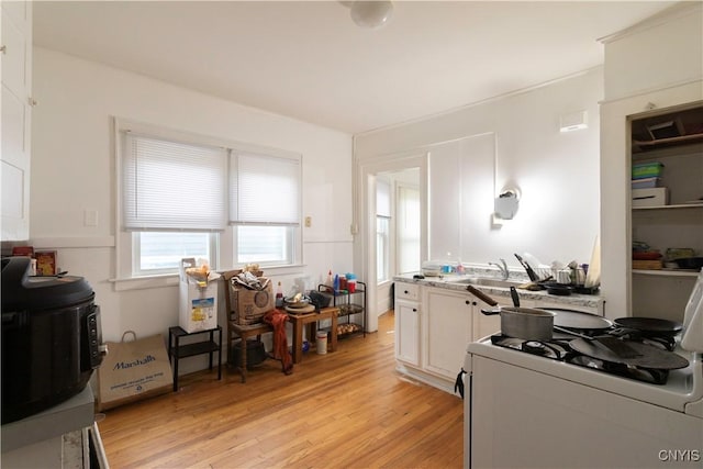 interior space with white gas stove, white cabinets, light wood-style floors, and a sink