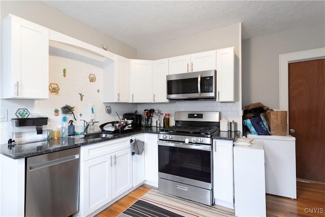 kitchen featuring a sink, stainless steel appliances, white cabinetry, and dark stone counters