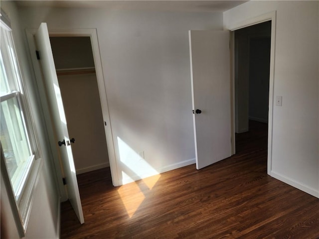 unfurnished bedroom with a closet, baseboards, and dark wood-type flooring